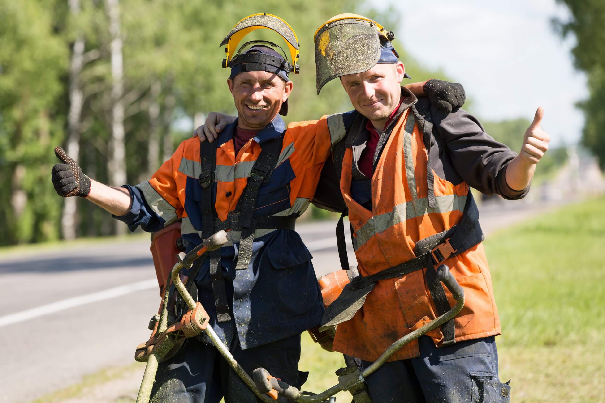 Happy road landscapers workers with string trimmers during grass cutting team works gesturing ok outdoors